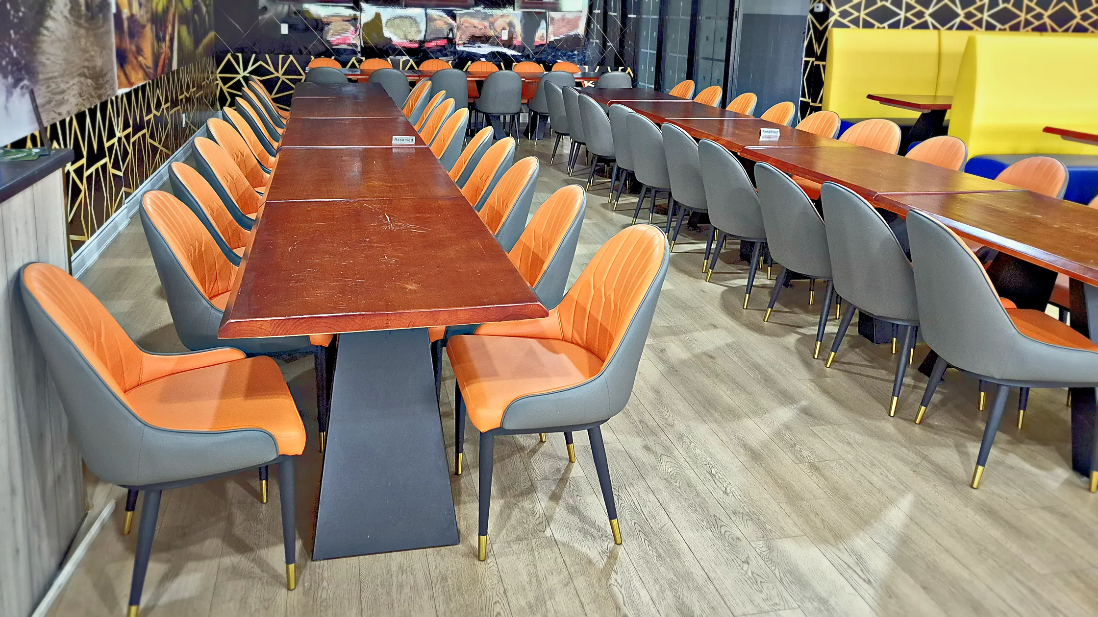Matka Biryani House dining room with long wooden tables, orange and grey chairs and a mural wall